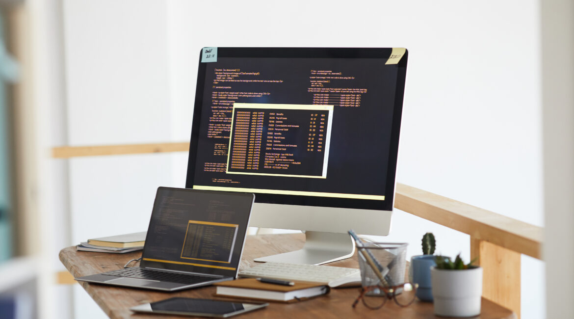 Background image of black and orange programming code on computer screen and digital devices in modern white office interior, copy space