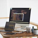 Background image of black and orange programming code on computer screen and digital devices in modern white office interior, copy space