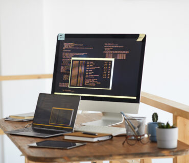Background image of black and orange programming code on computer screen and digital devices in modern white office interior, copy space